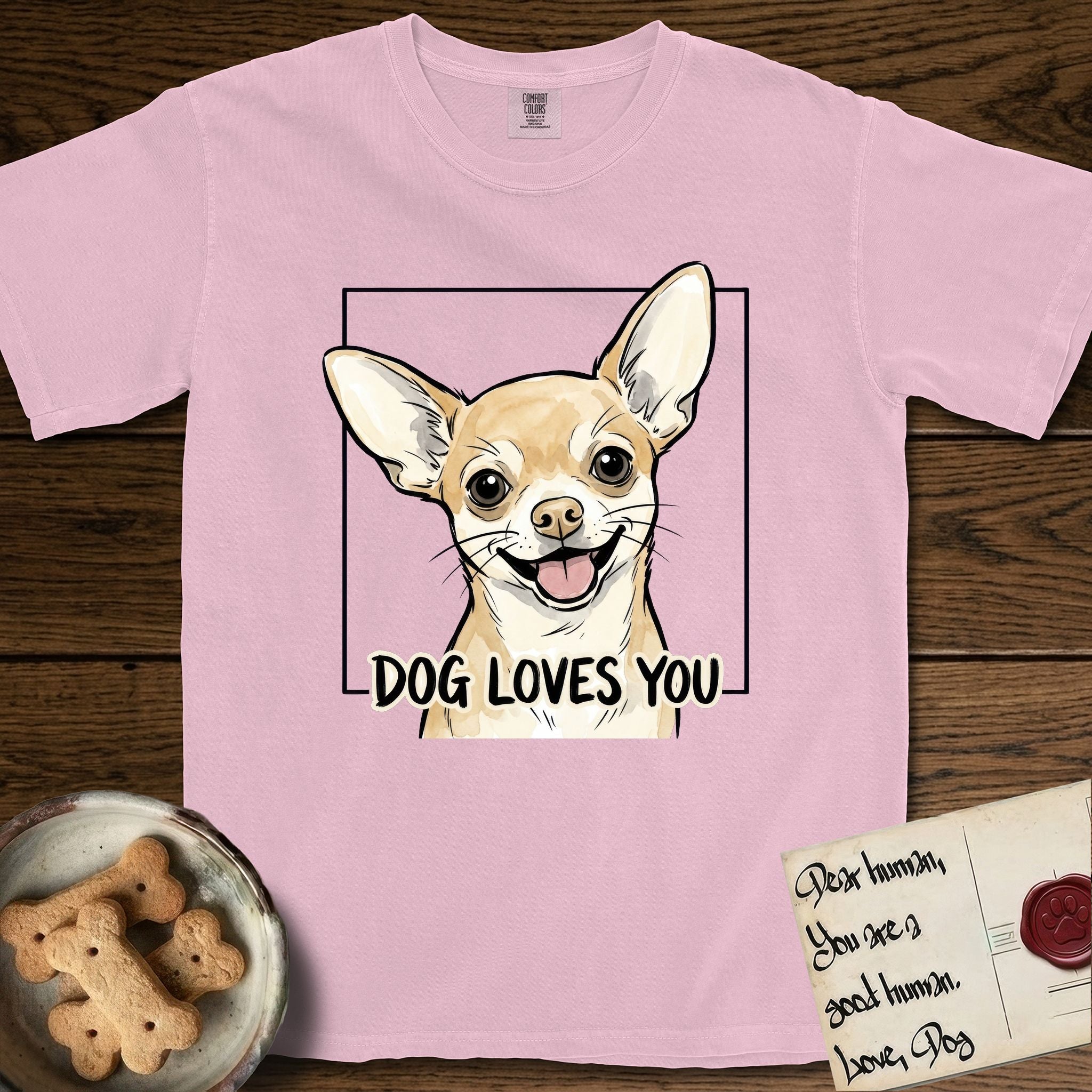 Dog Loves You Chihuahua T-Shirt flat lay in Blossom, featuring Ink and watercolor portrait of a smiling fawn Chihuahua with enormous upright bat ears and big round dark eyes, head tilted inside a black frame above hand-lettered text reading DOG LOVES YOU.