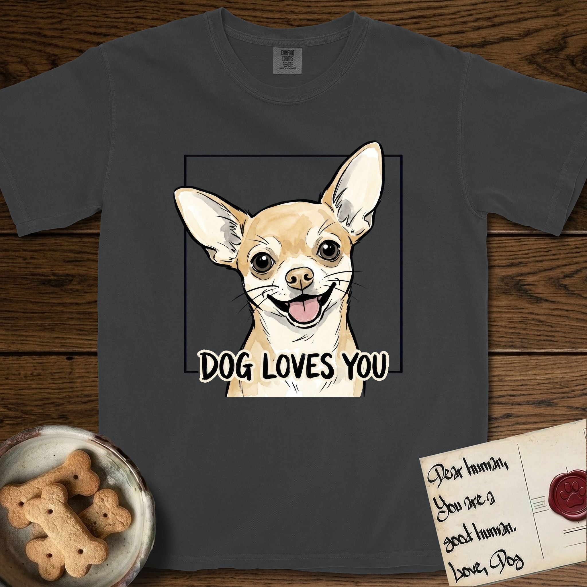 Dog Loves You Chihuahua T-Shirt flat lay in Graphite, featuring Ink and watercolor portrait of a smiling fawn Chihuahua with enormous upright bat ears and big round dark eyes, head tilted inside a black frame above hand-lettered text reading DOG LOVES YOU.