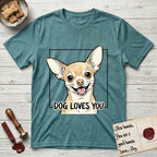 Dog Loves You Chihuahua T-Shirt flat lay in Heather Galapagos Blue, featuring Ink and watercolor portrait of a smiling fawn Chihuahua with enormous upright bat ears and big round dark eyes, head tilted inside a black frame above hand-lettered text reading DOG LOVES YOU.