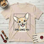 Dog Loves You Chihuahua T-Shirt flat lay in Sand, featuring Ink and watercolor portrait of a smiling fawn Chihuahua with enormous upright bat ears and big round dark eyes, head tilted inside a black frame above hand-lettered text reading DOG LOVES YOU.