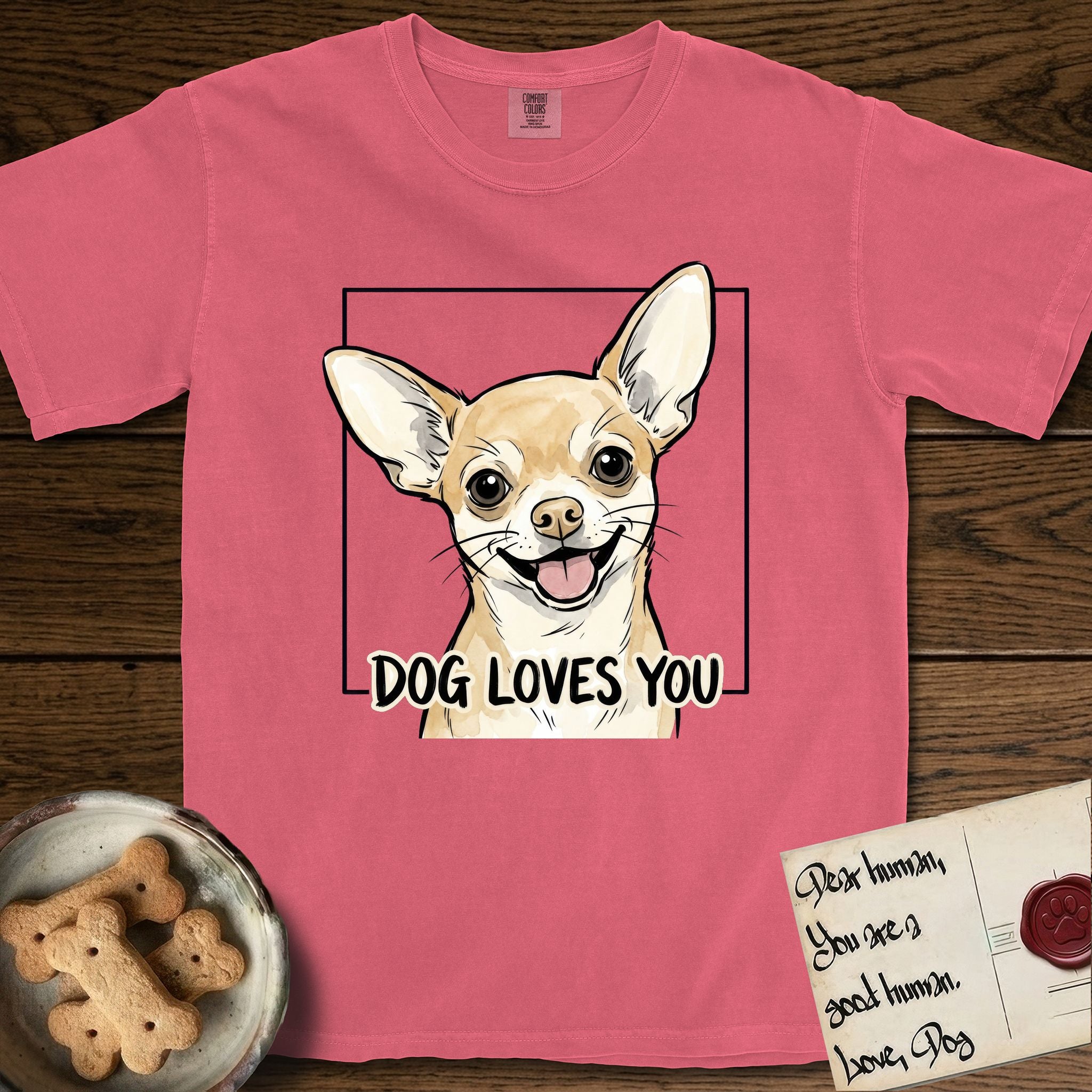 Dog Loves You Chihuahua T-Shirt flat lay in Watermelon, featuring Ink and watercolor portrait of a smiling fawn Chihuahua with enormous upright bat ears and big round dark eyes, head tilted inside a black frame above hand-lettered text reading DOG LOVES YOU.