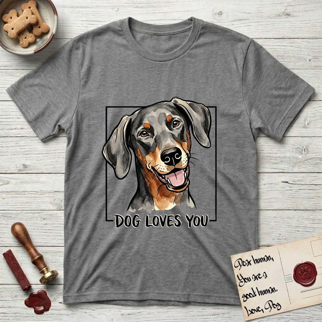 Dog Loves You Doberman T-Shirt flat lay in Graphite Heather, featuring Ink and watercolor portrait of a smiling black and rust Doberman with long natural hanging ears, head tilted inside a black frame above hand-lettered text reading DOG LOVES YOU.
