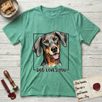Dog Loves You Doberman T-Shirt flat lay in Heather Irish Green, featuring Ink and watercolor portrait of a smiling black and rust Doberman with long natural hanging ears, head tilted inside a black frame above hand-lettered text reading DOG LOVES YOU.