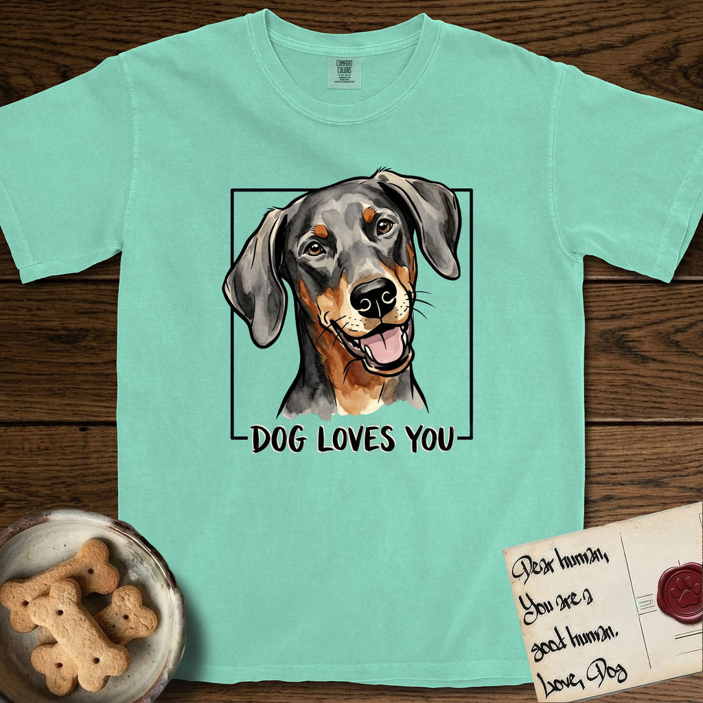 Dog Loves You Doberman T-Shirt flat lay in Island Reef, featuring Ink and watercolor portrait of a smiling black and rust Doberman with long natural hanging ears, head tilted inside a black frame above hand-lettered text reading DOG LOVES YOU.