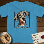 Dog Loves You Doberman T-Shirt flat lay in Royal Caribe, featuring Ink and watercolor portrait of a smiling black and rust Doberman with long natural hanging ears, head tilted inside a black frame above hand-lettered text reading DOG LOVES YOU.