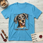 Dog Loves You Doberman T-Shirt flat lay in Sky, featuring Ink and watercolor portrait of a smiling black and rust Doberman with long natural hanging ears, head tilted inside a black frame above hand-lettered text reading DOG LOVES YOU.