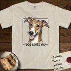 Dog Loves You Galgo T-Shirt flat lay in Ivory, featuring Ink and watercolor portrait of a smiling brindle Galgo with a long narrow muzzle and folded rose ears, head tilted inside a black frame above hand-lettered text reading DOG LOVES YOU.