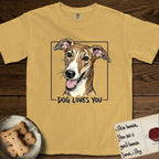 Dog Loves You Galgo T-Shirt flat lay in Mustard, featuring Ink and watercolor portrait of a smiling brindle Galgo with a long narrow muzzle and folded rose ears, head tilted inside a black frame above hand-lettered text reading DOG LOVES YOU.