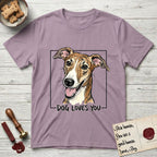 Dog Loves You Galgo T-Shirt flat lay in Paragon, featuring Ink and watercolor portrait of a smiling brindle Galgo with a long narrow muzzle and folded rose ears, head tilted inside a black frame above hand-lettered text reading DOG LOVES YOU.