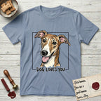 Dog Loves You Galgo T-Shirt flat lay in Stone Blue, featuring Ink and watercolor portrait of a smiling brindle Galgo with a long narrow muzzle and folded rose ears, head tilted inside a black frame above hand-lettered text reading DOG LOVES YOU.
