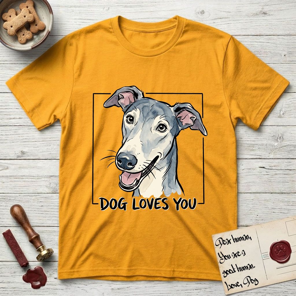 Dog Loves You Greyhound T-Shirt flat lay in Gold, featuring Ink and watercolor portrait of a smiling slate blue Greyhound with a long narrow muzzle, cream blaze and folded rose ears, head tilted inside a black frame above hand-lettered text reading DOG LOVES YOU.