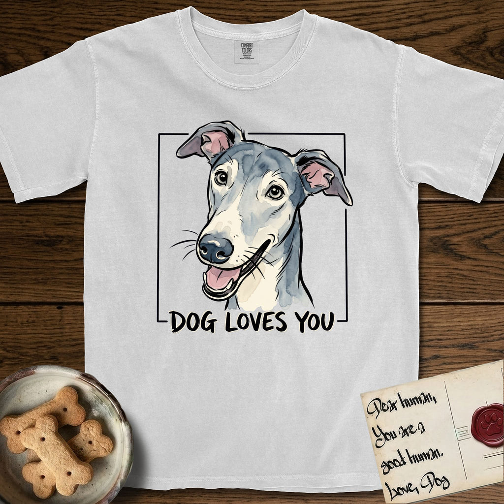Dog Loves You Greyhound T-Shirt flat lay in White, featuring Ink and watercolor portrait of a smiling slate blue Greyhound with a long narrow muzzle, cream blaze and folded rose ears, head tilted inside a black frame above hand-lettered text reading DOG LOVES YOU.