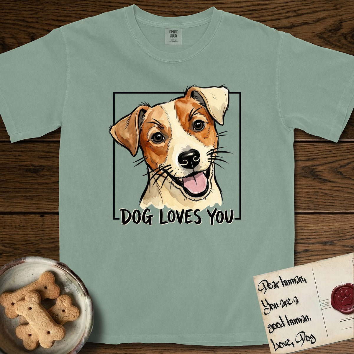 Dog Loves You Jack Russell T-Shirt flat lay in Bay, featuring Ink and watercolor portrait of a smiling cream and rust Jack Russell with folded button ears and keen dark eyes, head tilted inside a black frame above hand-lettered text reading DOG LOVES YOU.