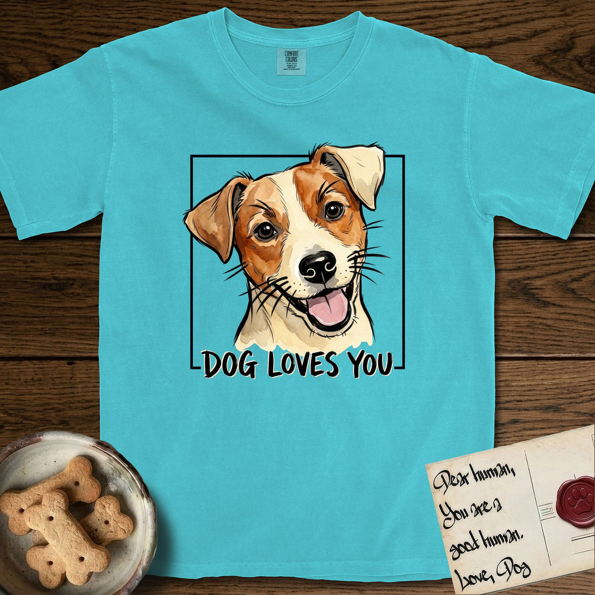 Dog Loves You Jack Russell T-Shirt flat lay in Lagoon Blue, featuring Ink and watercolor portrait of a smiling cream and rust Jack Russell with folded button ears and keen dark eyes, head tilted inside a black frame above hand-lettered text reading DOG LOVES YOU.