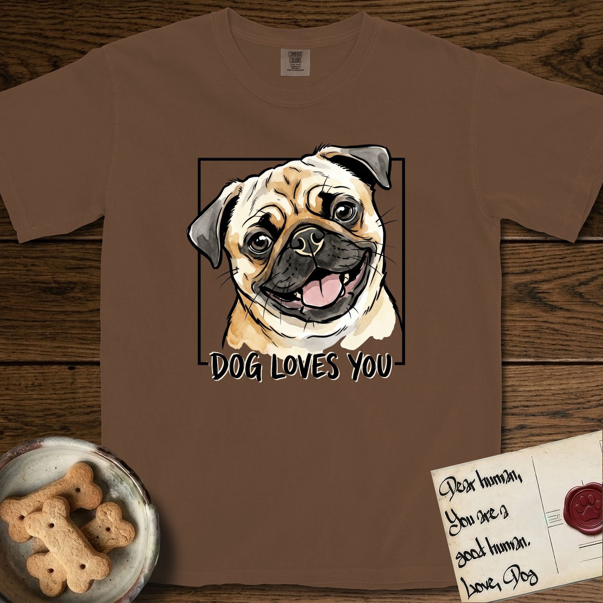 Dog Loves You Pug T-Shirt flat lay in Espresso, featuring Ink and watercolor portrait of a smiling fawn Pug with a black mask, deep brow wrinkles and big round eyes, head tilted inside a black frame above hand-lettered text reading DOG LOVES YOU.