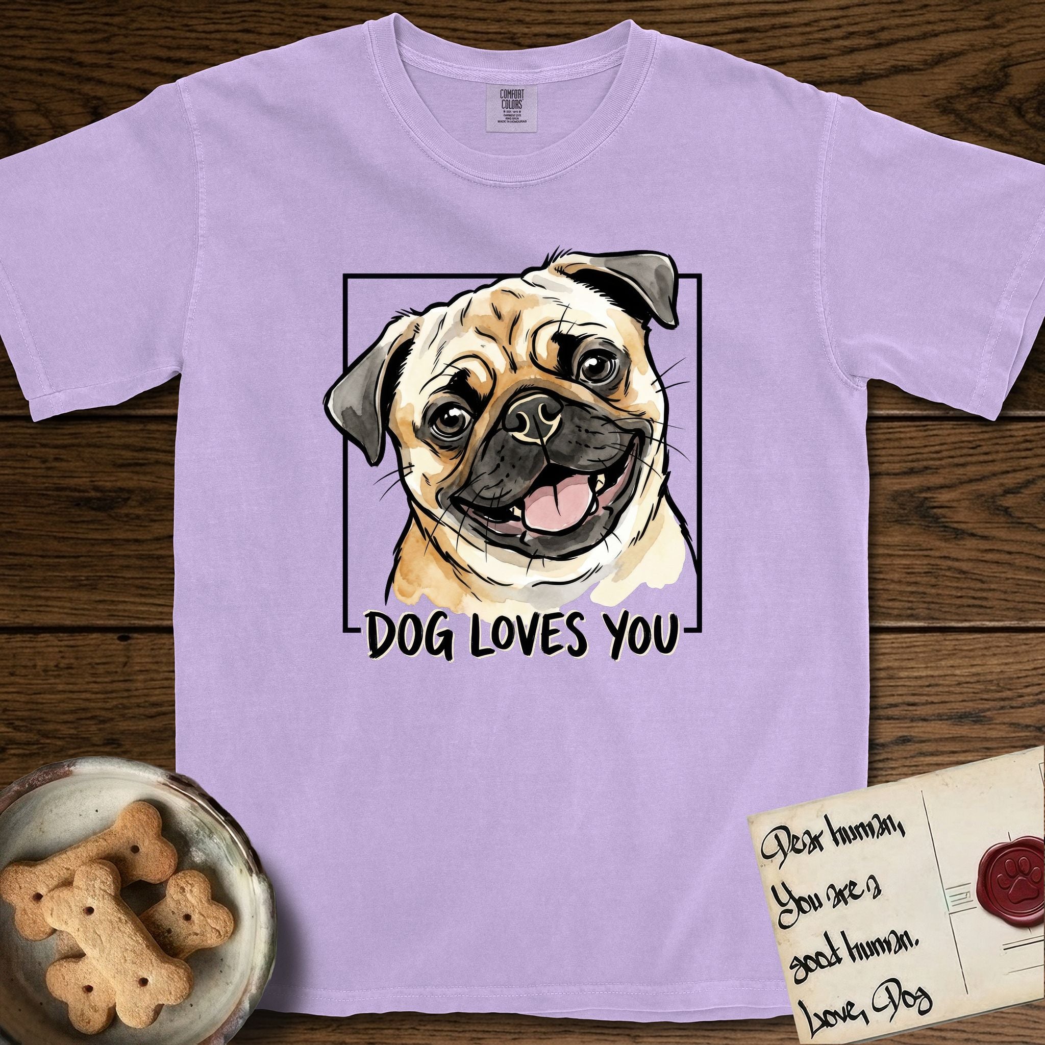 Dog Loves You Pug T-Shirt flat lay in Orchid, featuring Ink and watercolor portrait of a smiling fawn Pug with a black mask, deep brow wrinkles and big round eyes, head tilted inside a black frame above hand-lettered text reading DOG LOVES YOU.