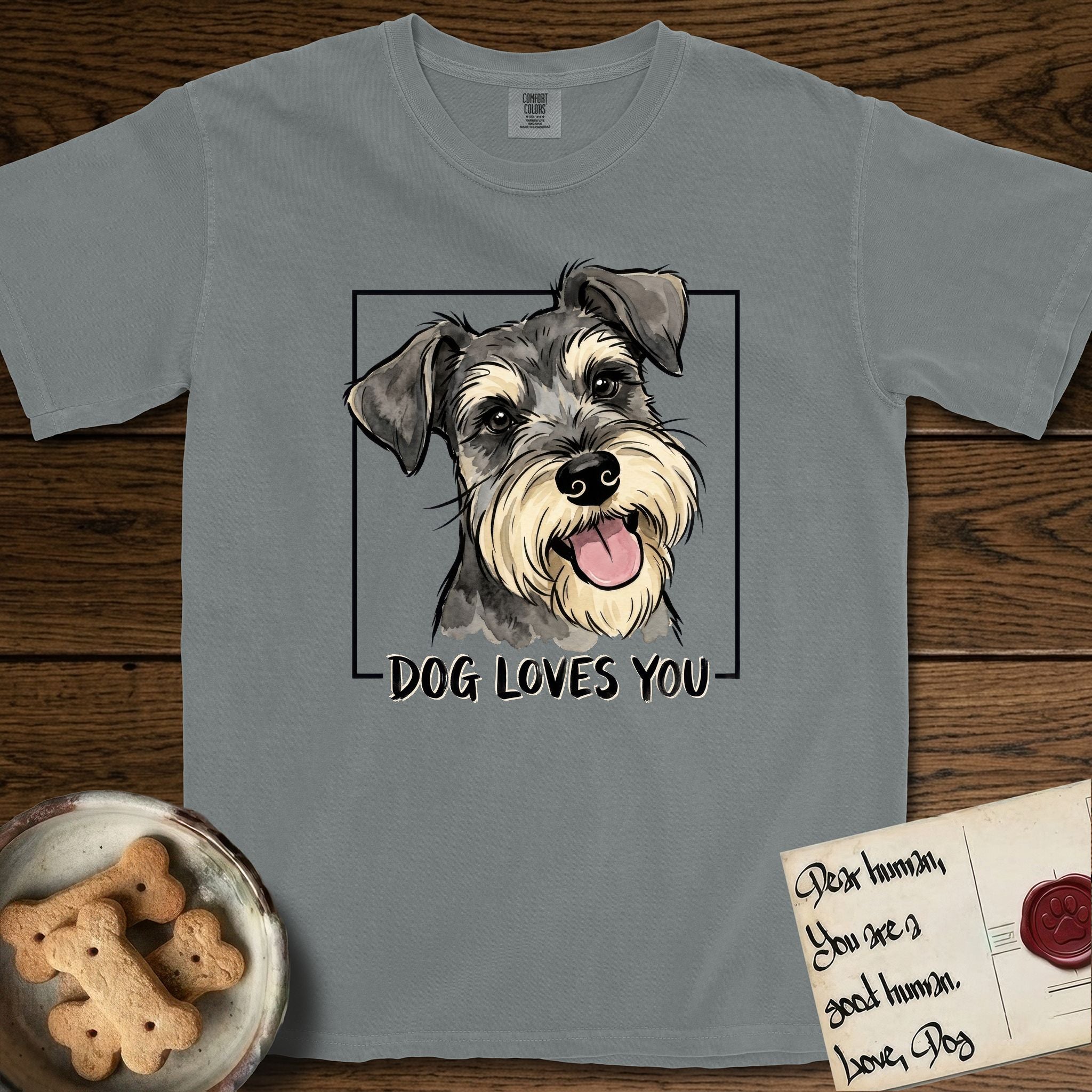 Dog Loves You Schnauzer T-Shirt flat lay in Granite, featuring Ink and watercolor portrait of a smiling salt and pepper Schnauzer with a long beard and bushy eyebrows, head tilted inside a black frame above hand-lettered text reading DOG LOVES YOU.