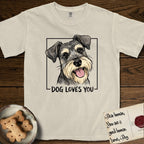 Dog Loves You Schnauzer T-Shirt flat lay in Ivory, featuring Ink and watercolor portrait of a smiling salt and pepper Schnauzer with a long beard and bushy eyebrows, head tilted inside a black frame above hand-lettered text reading DOG LOVES YOU.