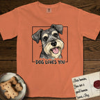 Dog Loves You Schnauzer T-Shirt flat lay in Melon, featuring Ink and watercolor portrait of a smiling salt and pepper Schnauzer with a long beard and bushy eyebrows, head tilted inside a black frame above hand-lettered text reading DOG LOVES YOU.