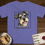 Dog Loves You Schnauzer T-Shirt flat lay in Violet, featuring Ink and watercolor portrait of a smiling salt and pepper Schnauzer with a long beard and bushy eyebrows, head tilted inside a black frame above hand-lettered text reading DOG LOVES YOU.