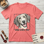 Dog Loves You Weimaraner T-Shirt flat lay in Coral Silk, featuring Ink and watercolor portrait of a smiling silver grey Weimaraner with long velvet hanging ears and pale amber eyes, head tilted inside a black frame above hand-lettered text reading DOG LOVES YOU.