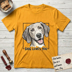 Dog Loves You Weimaraner T-Shirt flat lay in Gold, featuring Ink and watercolor portrait of a smiling silver grey Weimaraner with long velvet hanging ears and pale amber eyes, head tilted inside a black frame above hand-lettered text reading DOG LOVES YOU.