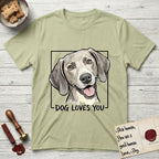 Dog Loves You Weimaraner T-Shirt flat lay in Pistachio, featuring Ink and watercolor portrait of a smiling silver grey Weimaraner with long velvet hanging ears and pale amber eyes, head tilted inside a black frame above hand-lettered text reading DOG LOVES YOU.