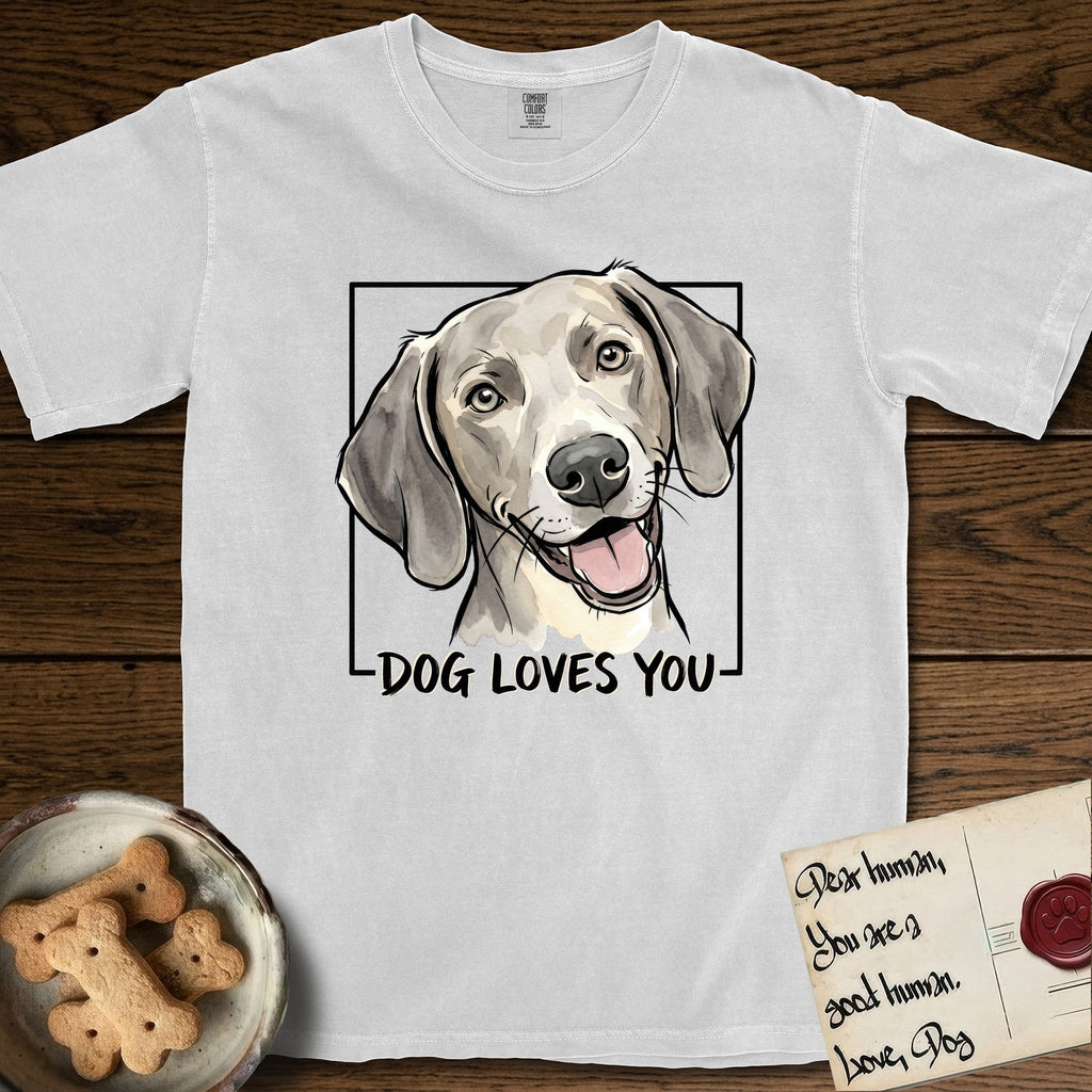 Dog Loves You Weimaraner T-Shirt flat lay in White, featuring Ink and watercolor portrait of a smiling silver grey Weimaraner with long velvet hanging ears and pale amber eyes, head tilted inside a black frame above hand-lettered text reading DOG LOVES YOU.