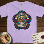 How Great Thou Bark Australian Shepherd T-Shirt flat lay in Orchid, featuring a full-color stained-glass saint window of a blue merle Australian Shepherd with one blue eye and one amber eye, haloed in golden light.