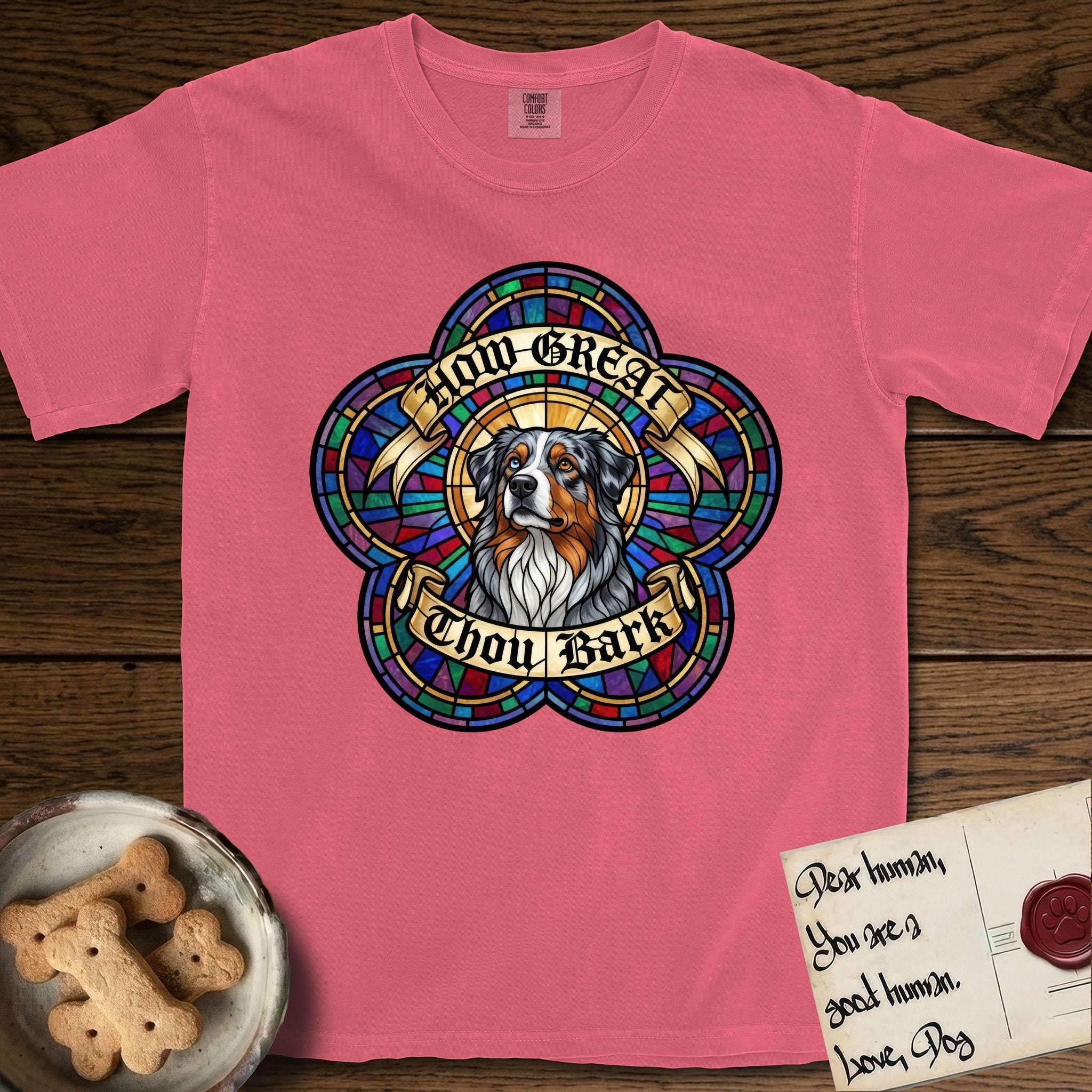 How Great Thou Bark Australian Shepherd T-Shirt flat lay in Watermelon, featuring a full-color stained-glass saint window of a blue merle Australian Shepherd with one blue eye and one amber eye, haloed in golden light.