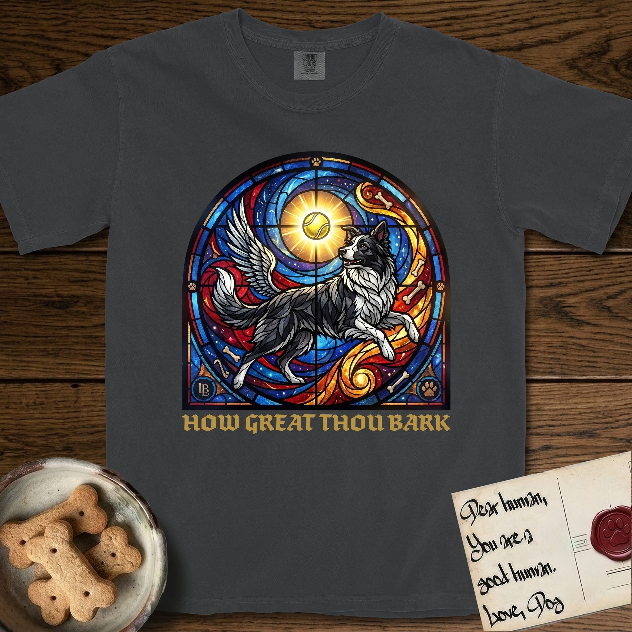 How Great Thou Bark Border Collie T-Shirt flat lay in Graphite, featuring a full-color stained-glass saint window of a winged Border Collie leaping after a glowing tennis ball, with a halo.