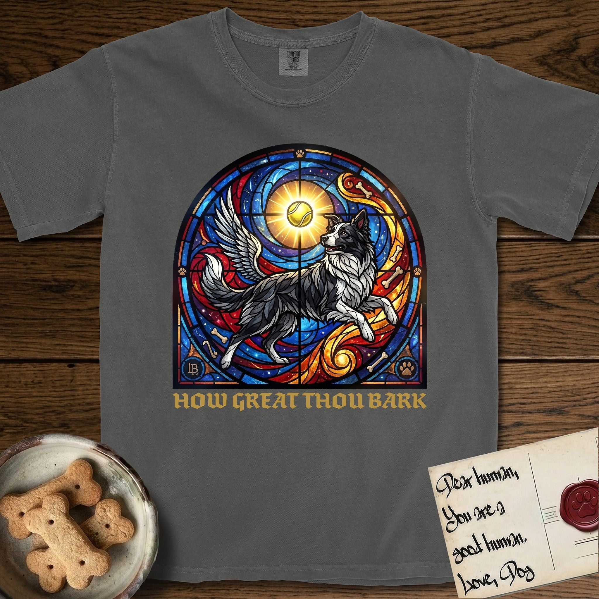 How Great Thou Bark Border Collie T-Shirt flat lay in Pepper, featuring a full-color stained-glass saint window of a winged Border Collie leaping after a glowing tennis ball, with a halo.