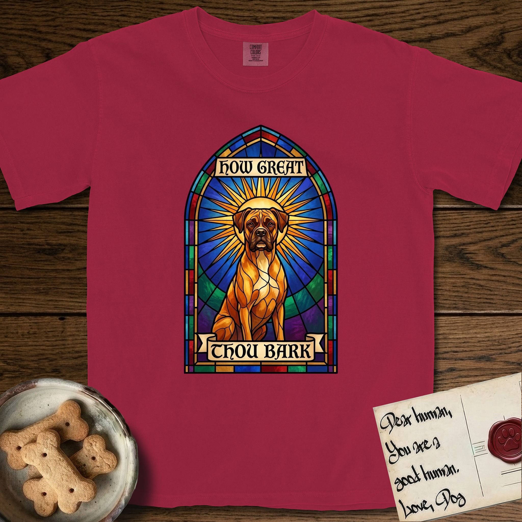 How Great Thou Bark Boxer T-Shirt flat lay in Chili, featuring a full-color stained-glass saint window of a Boxer seated in warm golden light with a halo.