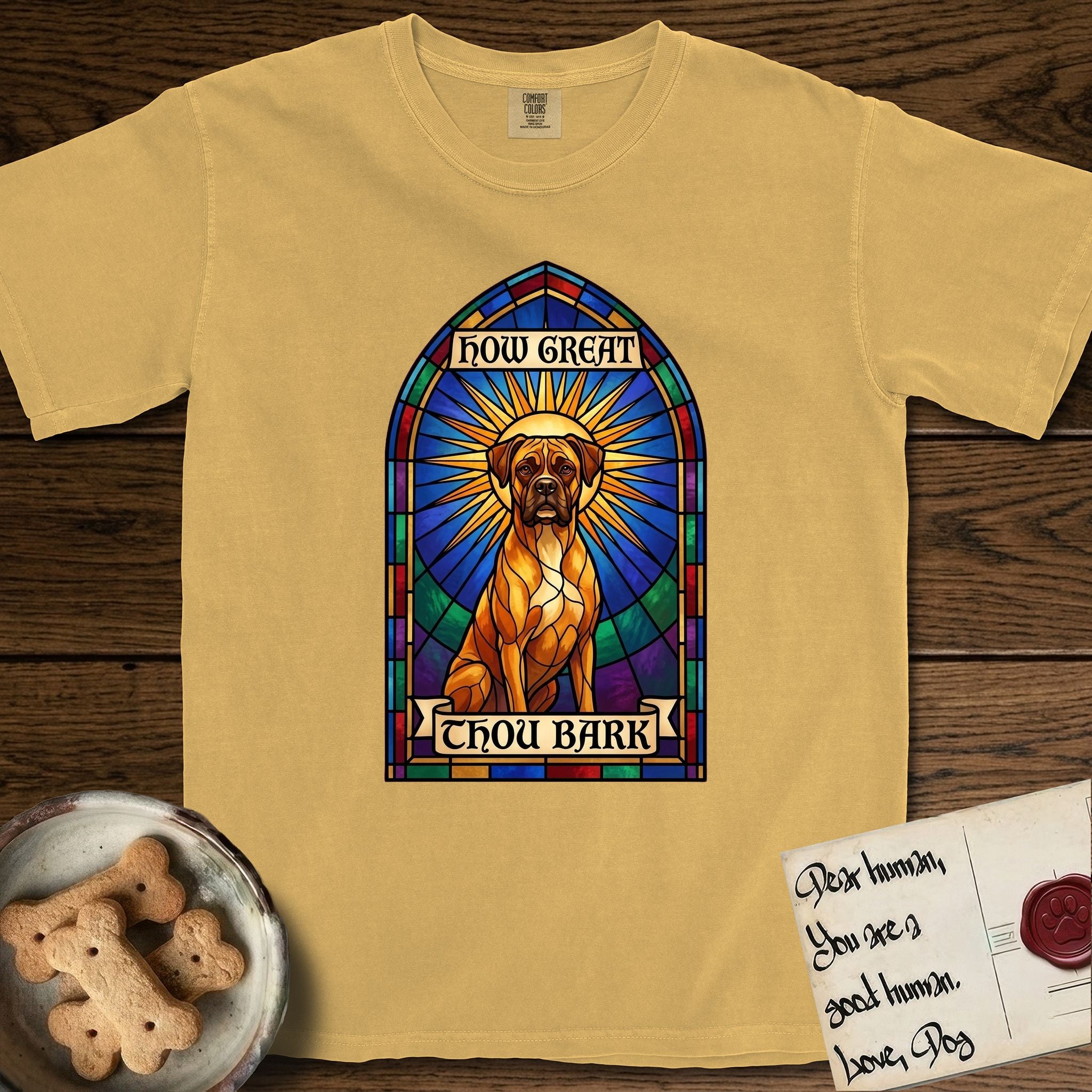 How Great Thou Bark Boxer T-Shirt flat lay in Mustard, featuring a full-color stained-glass saint window of a Boxer seated in warm golden light with a halo.