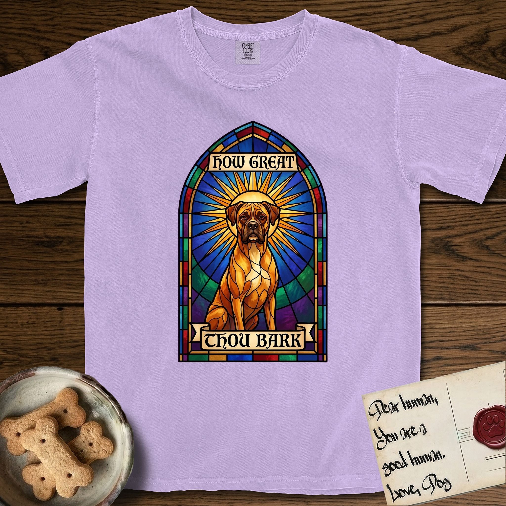 How Great Thou Bark Boxer T-Shirt flat lay in Orchid, featuring a full-color stained-glass saint window of a Boxer seated in warm golden light with a halo.