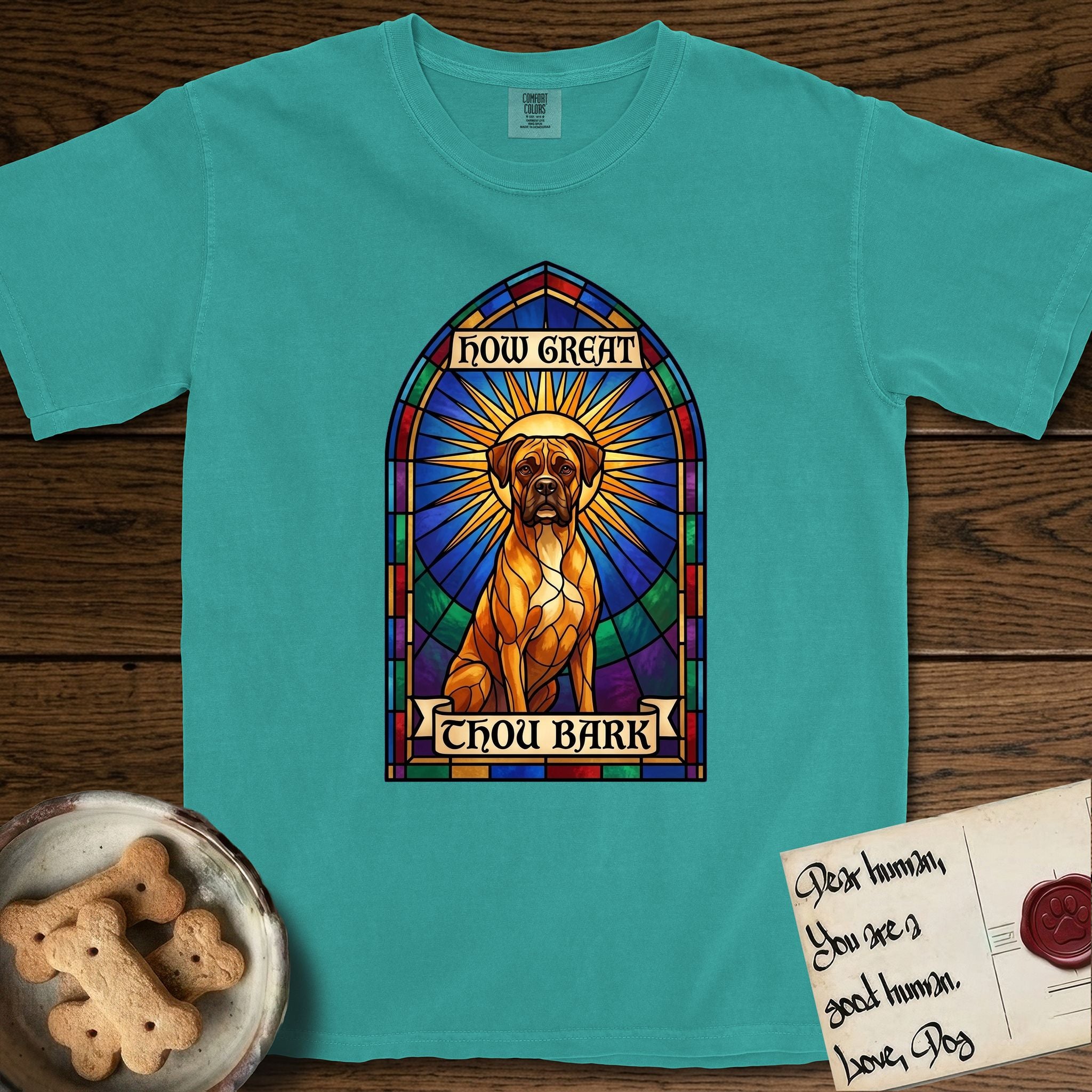 How Great Thou Bark Boxer T-Shirt flat lay in Seafoam, featuring a full-color stained-glass saint window of a Boxer seated in warm golden light with a halo.
