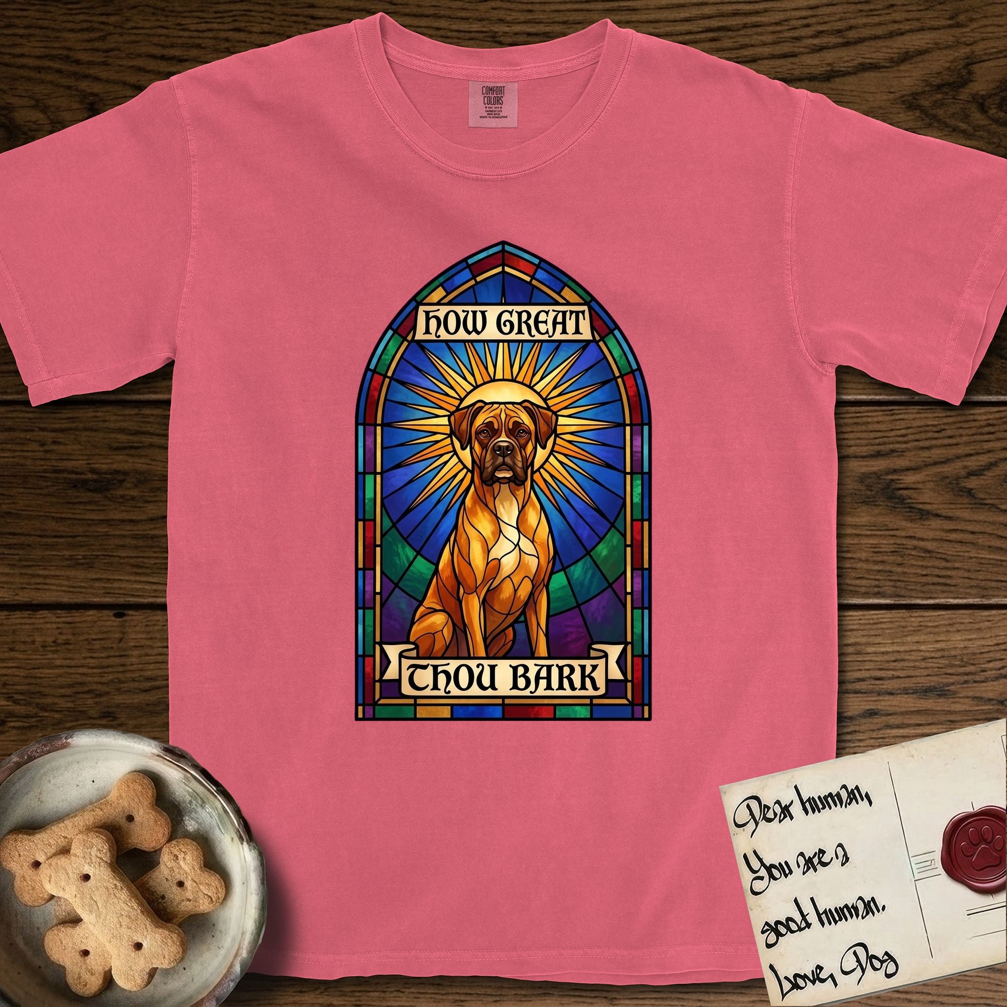 How Great Thou Bark Boxer T-Shirt flat lay in Watermelon, featuring a full-color stained-glass saint window of a Boxer seated in warm golden light with a halo.