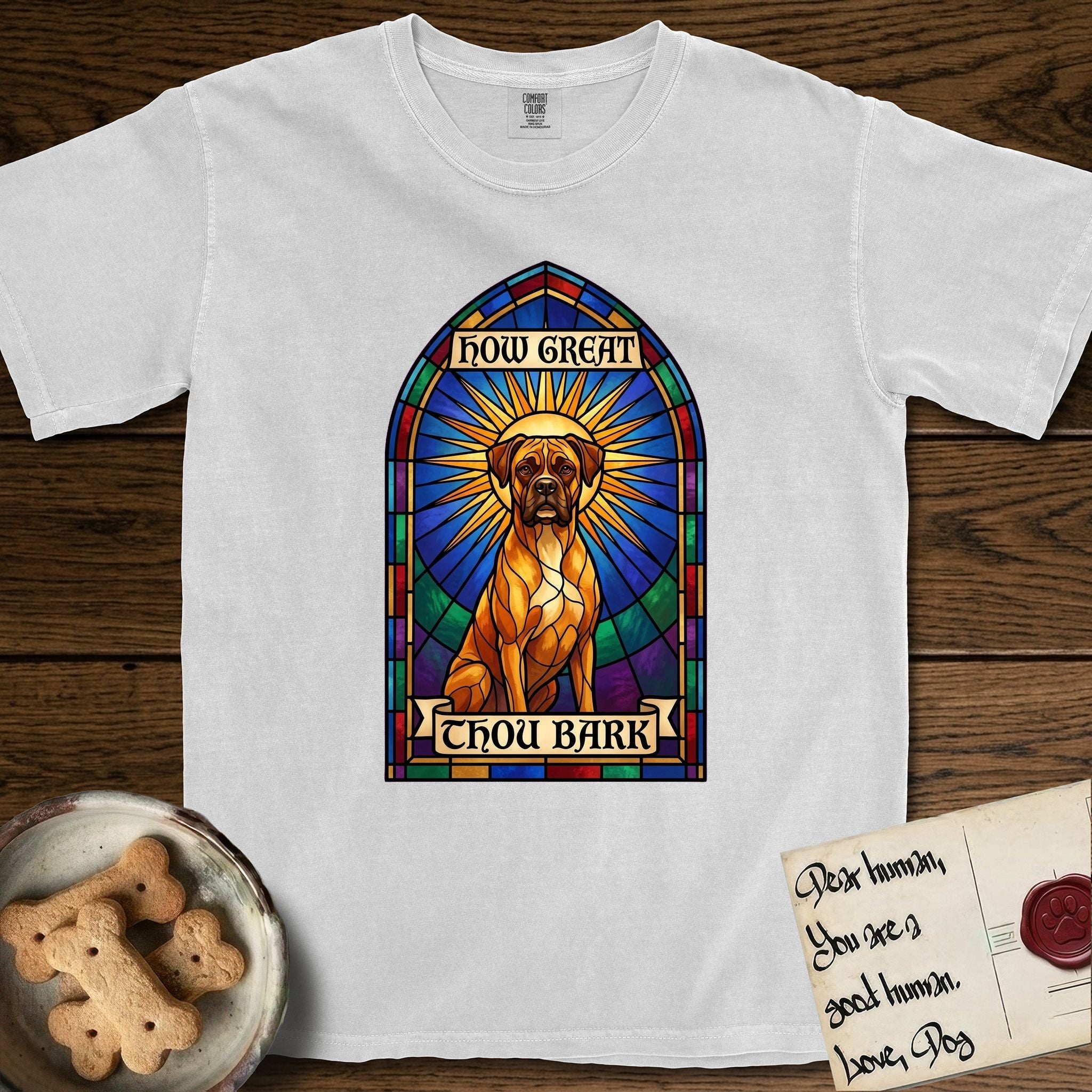 How Great Thou Bark Boxer T-Shirt flat lay in White, featuring a full-color stained-glass saint window of a Boxer seated in warm golden light with a halo.