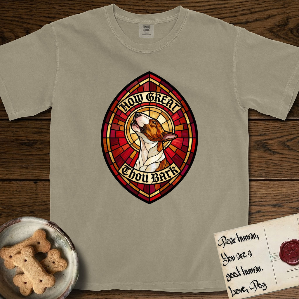 How Great Thou Bark Bull Terrier T-Shirt flat lay in Khaki, featuring a full-color stained-glass saint window of a brown and white Bull Terrier with head raised and mouth open mid-howl, haloed in golden light.