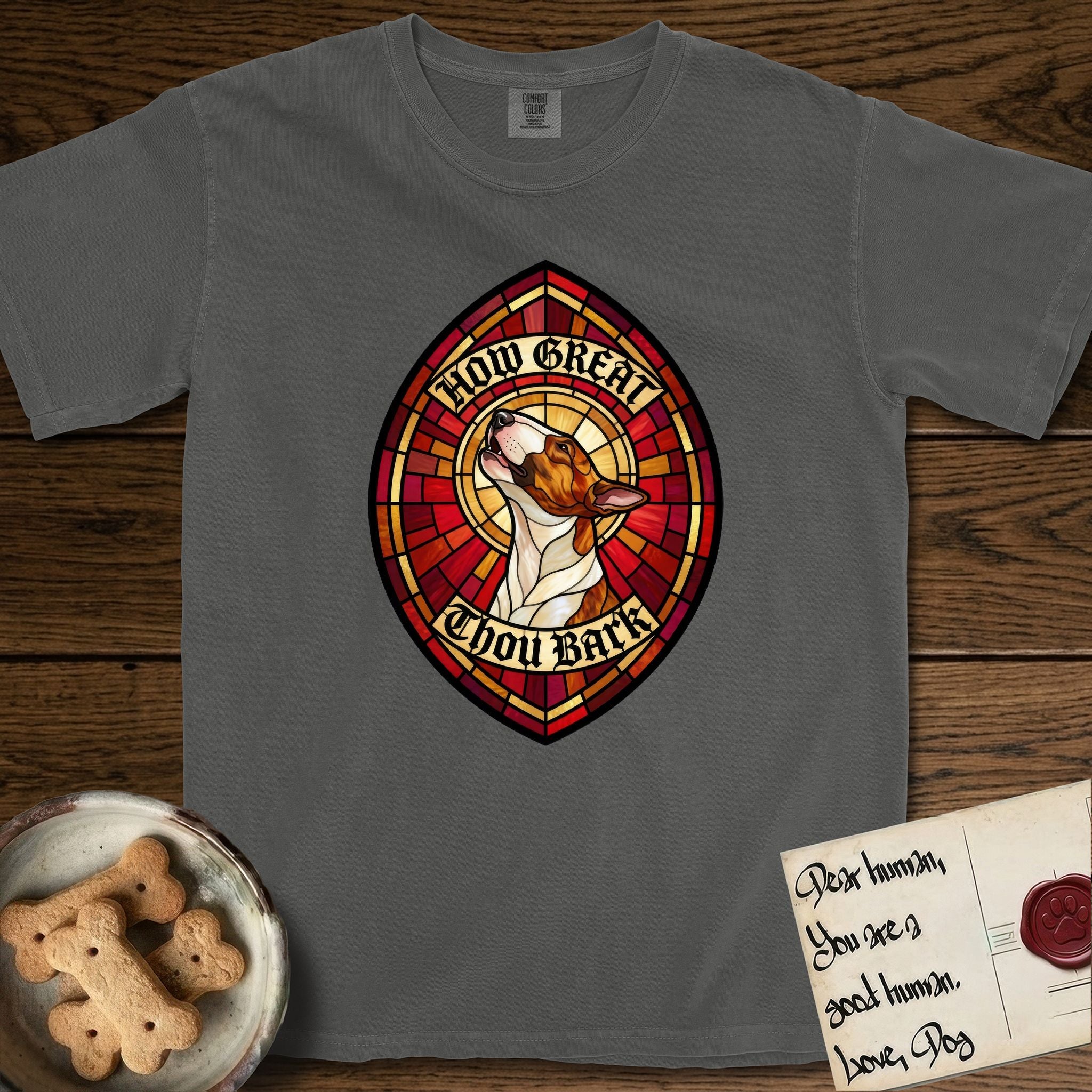 How Great Thou Bark Bull Terrier T-Shirt flat lay in Pepper, featuring a full-color stained-glass saint window of a brown and white Bull Terrier with head raised and mouth open mid-howl, haloed in golden light.