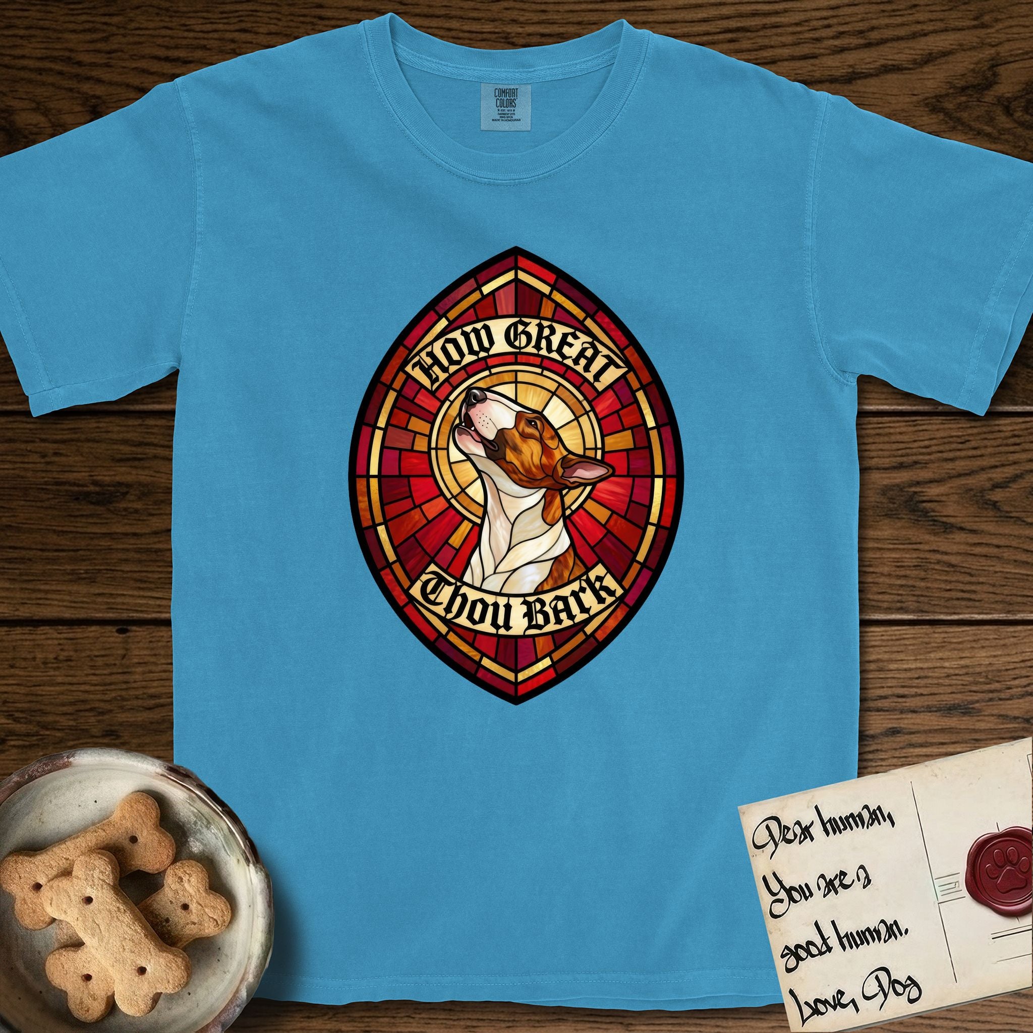 How Great Thou Bark Bull Terrier T-Shirt flat lay in Royal Caribe, featuring a full-color stained-glass saint window of a brown and white Bull Terrier with head raised and mouth open mid-howl, haloed in golden light.