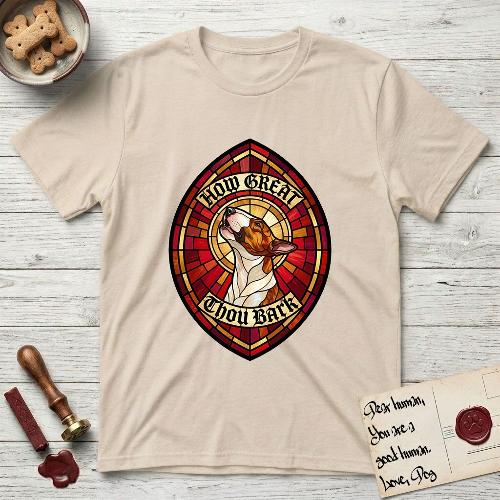How Great Thou Bark Bull Terrier T-Shirt flat lay in Sand, featuring a full-color stained-glass saint window of a brown and white Bull Terrier with head raised and mouth open mid-howl, haloed in golden light.