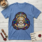 How Great Thou Bark Coton de Tulear T-Shirt flat lay in Carolina Blue, featuring a full-color stained-glass saint window of a sable and white Coton de Tulear facing forward, haloed in golden light.