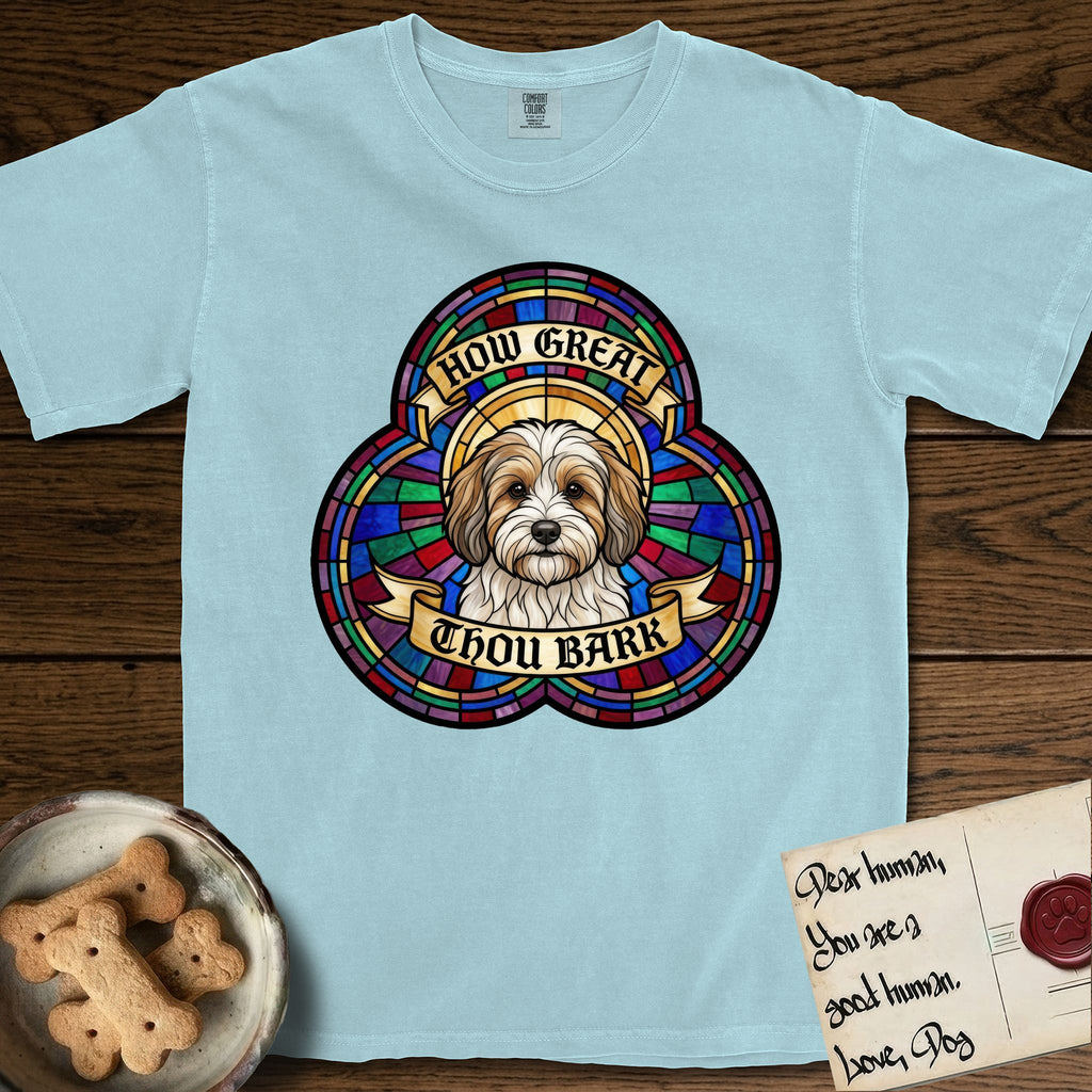 How Great Thou Bark Coton de Tulear T-Shirt flat lay in Chambray, featuring a full-color stained-glass saint window of a sable and white Coton de Tulear facing forward, haloed in golden light.