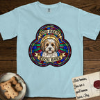 How Great Thou Bark Coton de Tulear T-Shirt flat lay in Chambray, featuring a full-color stained-glass saint window of a sable and white Coton de Tulear facing forward, haloed in golden light.