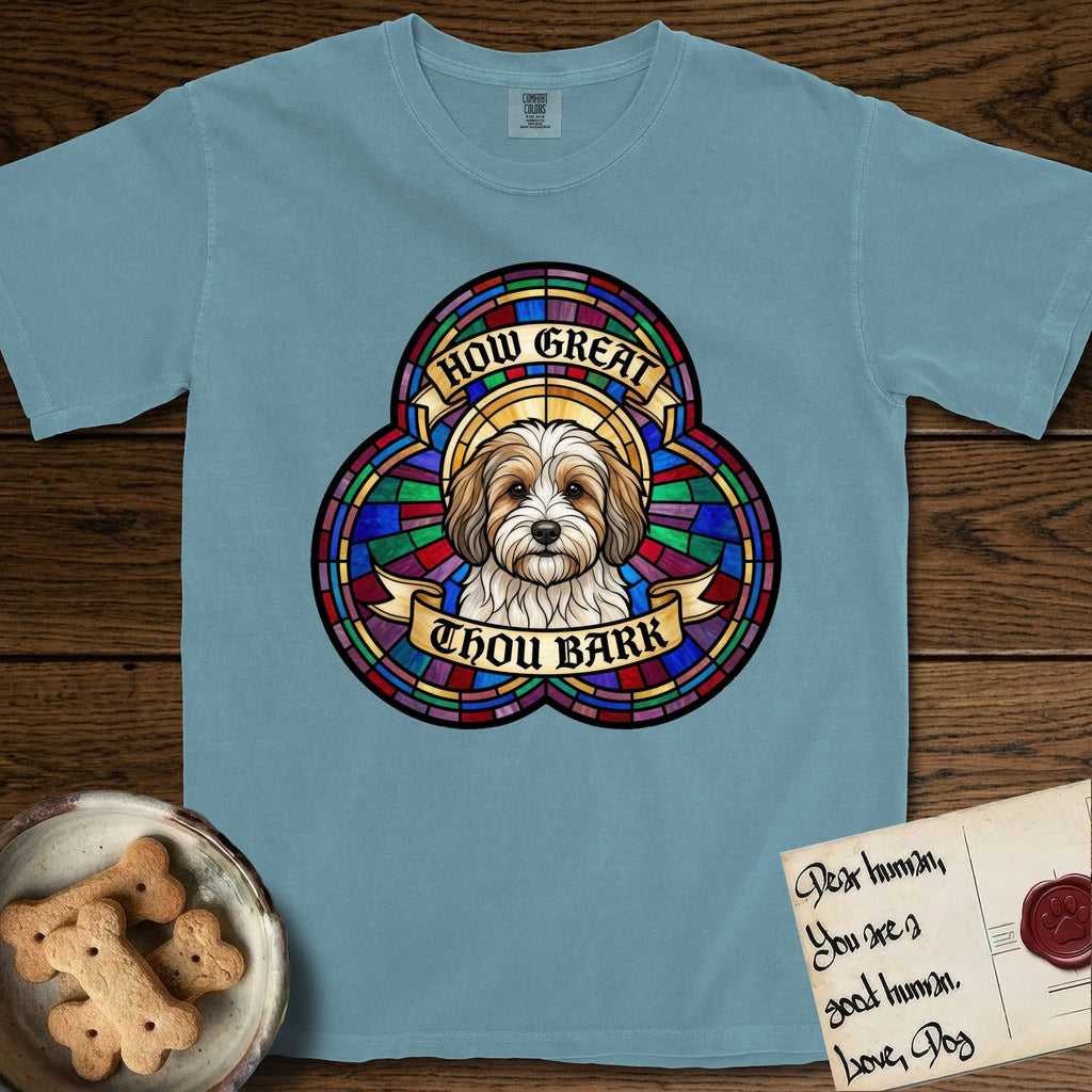 How Great Thou Bark Coton de Tulear T-Shirt flat lay in Ice Blue, featuring a full-color stained-glass saint window of a sable and white Coton de Tulear facing forward, haloed in golden light.