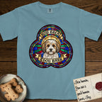 How Great Thou Bark Coton de Tulear T-Shirt flat lay in Ice Blue, featuring a full-color stained-glass saint window of a sable and white Coton de Tulear facing forward, haloed in golden light.
