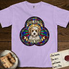 How Great Thou Bark Coton de Tulear T-Shirt flat lay in Orchid, featuring a full-color stained-glass saint window of a sable and white Coton de Tulear facing forward, haloed in golden light.
