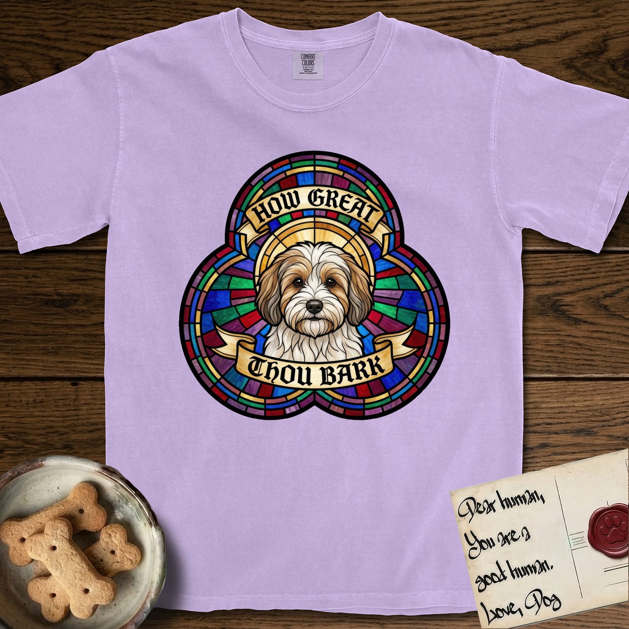How Great Thou Bark Coton de Tulear T-Shirt flat lay in Orchid, featuring a full-color stained-glass saint window of a sable and white Coton de Tulear facing forward, haloed in golden light.