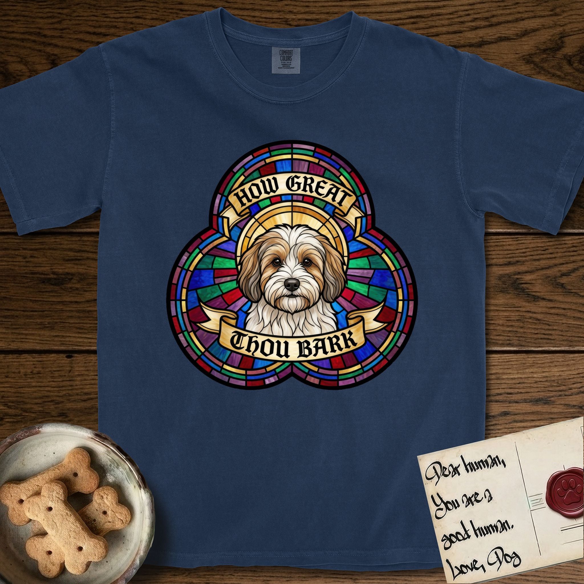 How Great Thou Bark Coton de Tulear T-Shirt flat lay in True Navy, featuring a full-color stained-glass saint window of a sable and white Coton de Tulear facing forward, haloed in golden light.
